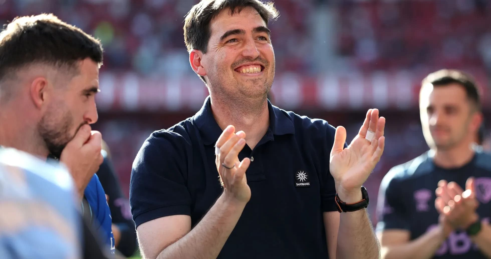 Entrenador aplaudiendo junto a jugadores en el estadio