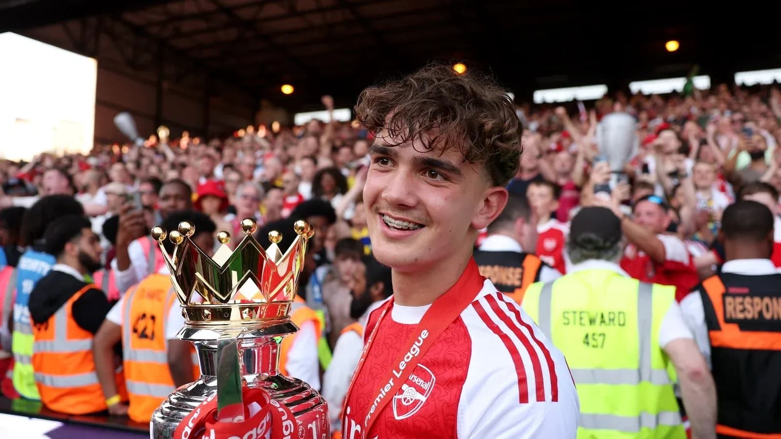 Jugador sosteniendo trofeo de la Premier League rodeado de aficionados