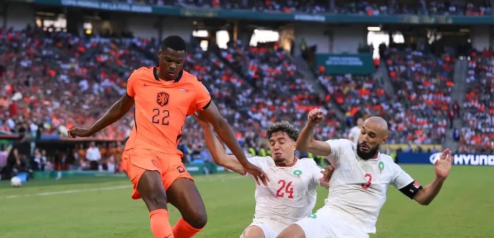Jugador de Países Bajos driblando entre dos defensores marroquíes